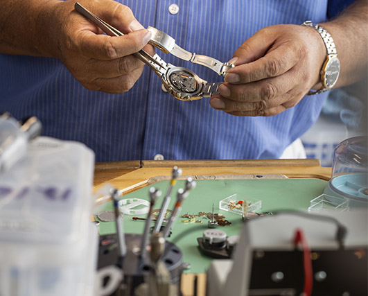 Hombre con un reloj en las manos frente a una mesa con diferentes herramientas de reparacion de relojes