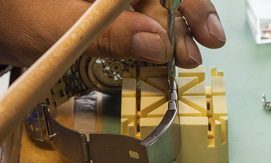 Reloj plateado sobre una herramienta color amarillo ajustando la correa con un desarmador plateado